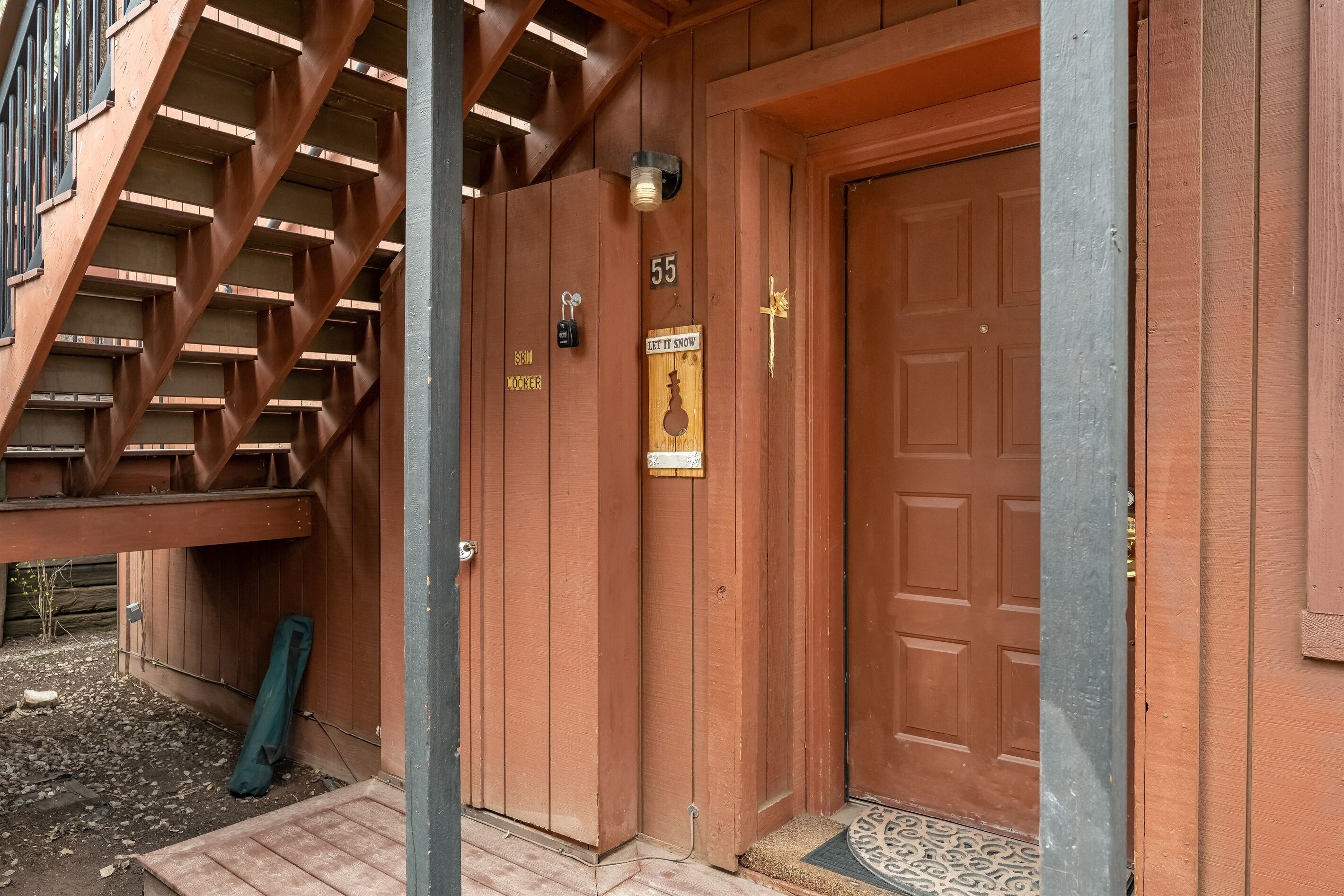 A wooden building with a staircase, a door marked with the number 55, and a 'Let It Snow' sign.