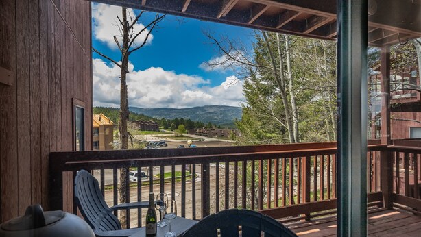 A wooden deck with a table and chairs, overlooking a street and mountains. - 3-Min Walk to Ski Lift | Mountain-View Chalet (Angel Fire)