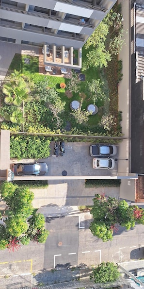 An aerial view of a residential area with a parking lot, a small garden with seating, and a multi-story building with balconies.