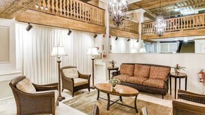 A spacious living room with a high ceiling, a large sofa, two armchairs, a coffee table, and a chandelier.