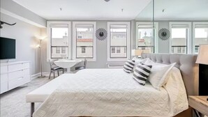 A bedroom with a bed, bedside table, lamp, and a desk with a chair.