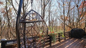 A wooden deck with a metal swing, a barbecue grill, and a bench.