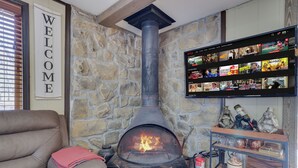 A stone wall with a fireplace, a couch, a TV mounted on the wall, and a shelf with various items.