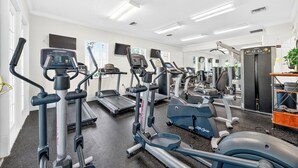 Ein Fitnessraum mit verschiedenen Cardiogeräten, einem Spiegel und einem Kühlschrank.