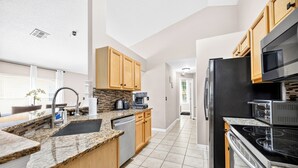 Eine moderne Küche mit Granitarbeitsplatten, Holzschränken, einem Edelstahlkühlschrank und einem eingebauten Backofen.