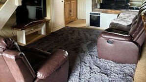 A cozy living room with a brown leather sofa, a flat-screen TV on a wooden stand, a large window, and a ceiling with exposed beams. - Mountain Condo - 4 Beds with 2 Bath - Prime Location (Mammoth Lakes)