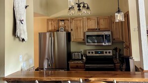 A kitchen with wooden cabinets, stainless steel appliances, a central island with bar stools, and pendant lighting. - Mountain Condo - 4 Beds with 2 Bath - Prime Location (Mammoth Lakes)