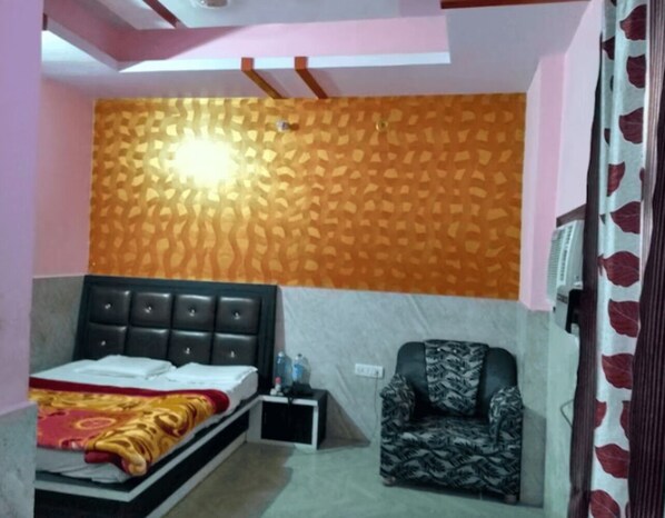A bedroom with a bed, a chair, a small table, and a patterned wall. - Hotel Park View (Kanpur)
