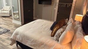 Et moderne soveværelse med en stor seng, et fjernsyn ophængt på væggen og et natbord med en lampe.