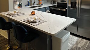 Et moderne køkken med en marmorø, rustfrie stålapparater, hængende lamper og barstole.
