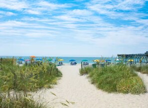 A beach path leading to the ocean with beach umbrellas and a pier. - Newly built 4BR, Steps to Beach, Grill/Balcony, Smart TVs & near SkyWheel! (Myrtle Beach)