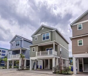 A row of two-story townhouses with a balcony on the second floor, a covered front porch, and a garage on the right. - Newly built 4BR, Steps to Beach, Grill/Balcony, Smart TVs & near SkyWheel! (Myrtle Beach)