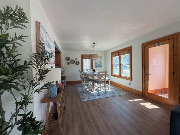 A spacious living area with a dining table, wooden flooring, and large windows.