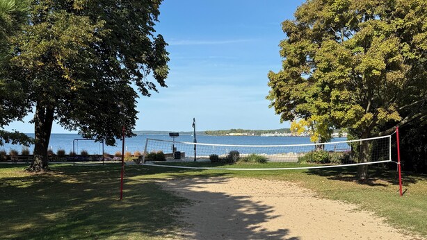 Een strandvolleybalveld met een net, omringd door bomen en uitzicht op zee.