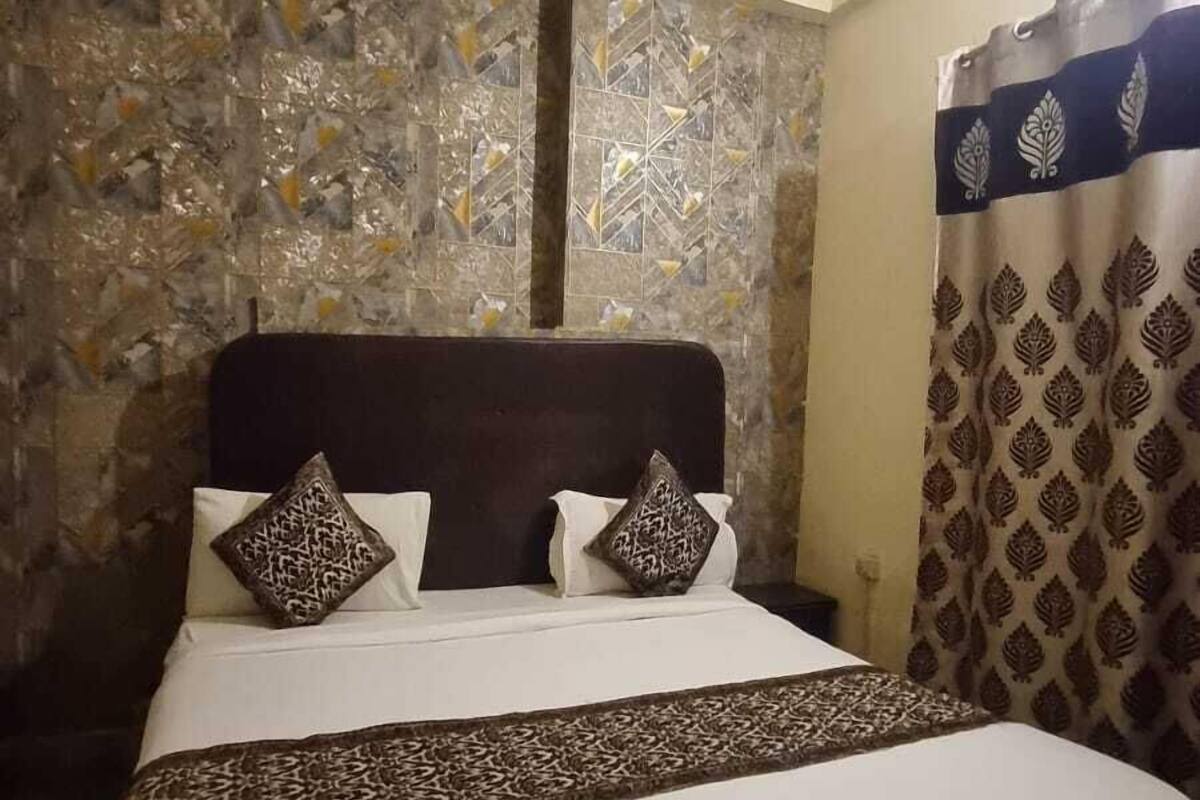 Una cama con cabecera estampada, pared decorativa y cortina con diseño de hojas.