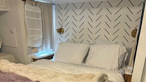 Uma cama com cabeceira branca, manta rosa fofa e lençol estampado com flores.