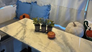 Uma cozinha compacta com bancada de mármore, três plantas em vasos, uma abóbora decorativa e uma almofada azul.
