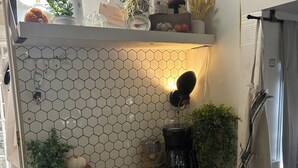 Uma cozinha com painel de azulejos hexagonais, uma cafeteira, um vaso de planta e um lustre.