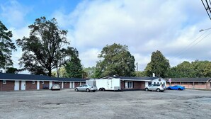 A motel with multiple rooms, a parking lot, and a small building in the background. - Your home away from home (Rocky Mount)
