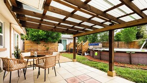 Een overdekt terras met een houten pergola, zitplaatsen buiten en een barbecuehoek.