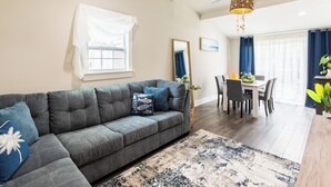 Een moderne woonkamer met een grijze modulaire bank, een eethoek met een witte tafel en stoelen, en een plafondventilator.