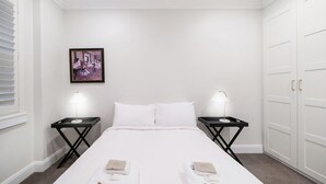 Ein Hotelzimmer mit einem Bett, zwei Nachttischen mit Lampen, einem gerahmten Bild an der Wand und einem Kleiderschrank.