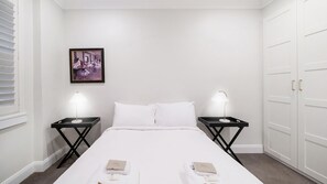 Une chambre d’hôtel avec un lit, deux tables de chevet avec des lampes, un tableau encadré au mur et une armoire.