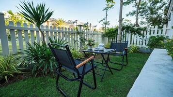 An outdoor patio area with two black chairs and a table, surrounded by a white picket fence and greenery.