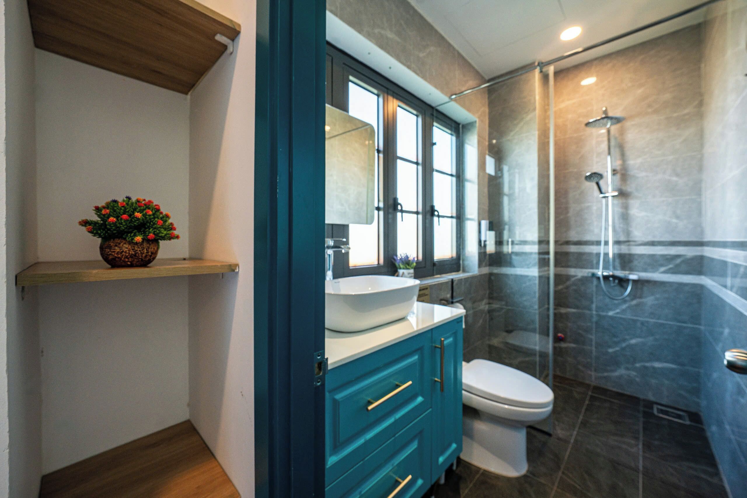A modern bathroom with a glass-enclosed shower, a white toilet, and a teal vanity with a bowl sink.