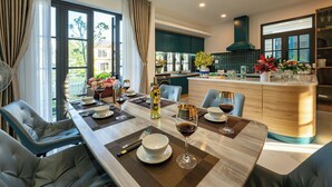 A modern dining area with a long table, chairs, and a kitchen in the background.