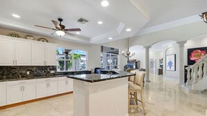 A spacious kitchen with white cabinetry, a granite countertop, and a central island. - Spacious 4 bedroom Coastal Luxury Retreat with Private Dock. (Marco Island)