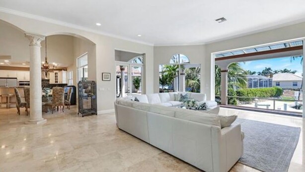 A spacious living area with a large white sectional sofa, a dining table with chairs, and a kitchen in the background. - Spacious 4 bedroom Coastal Luxury Retreat with Private Dock. (Marco Island)