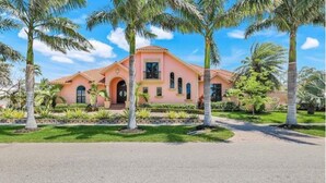 A two-story house with a pink facade, a central entrance with a black door, and a small balcony. - Spacious 4 bedroom Coastal Luxury Retreat with Private Dock. (Marco Island)