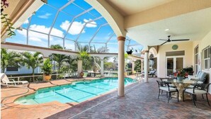 A covered outdoor swimming pool with a glass ceiling, surrounded by lounge chairs and a dining area. - Spacious 4 bedroom Coastal Luxury Retreat with Private Dock. (Marco Island)
