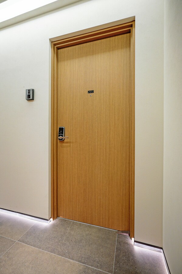 Une porte en bois dotée d’un clavier numérique, d’une petite lumière au-dessus de la porte et d’un sol carrelé.