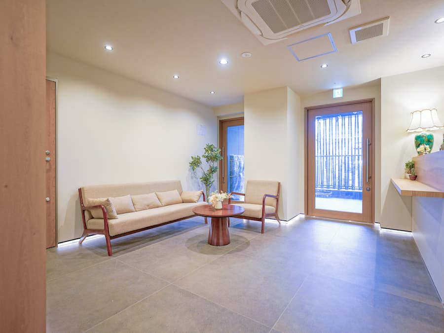 Un salon moderne avec un canapé beige, deux fauteuils, une table basse et un meuble en bois sur lequel est posée une lampe.
