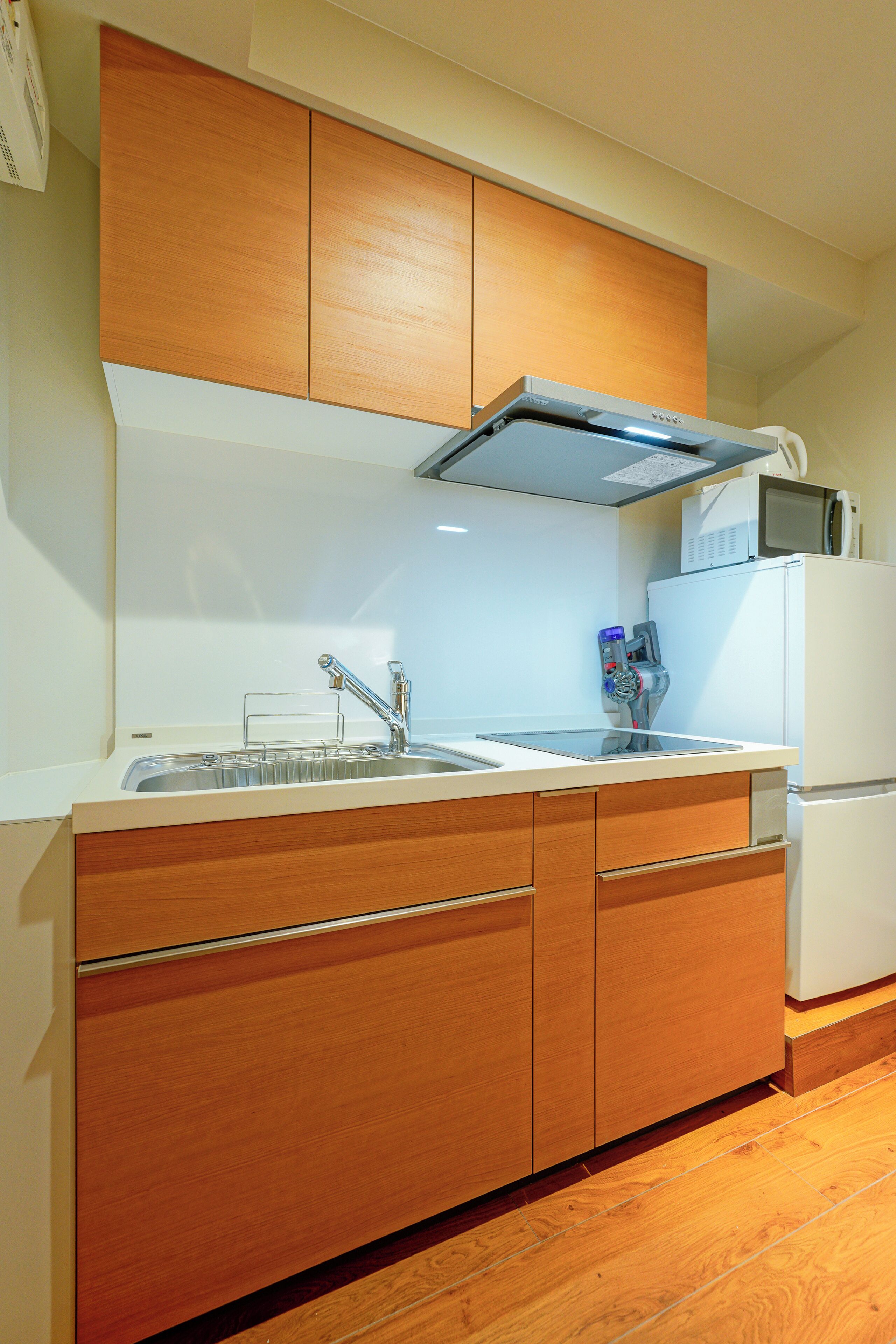 A compact kitchen with wooden cabinets, a stainless steel sink, and a microwave.