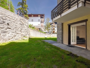 A modern building with a stone wall, a grassy area, and a balcony with a view of other buildings.