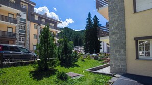 Edificio residencial con fachada de piedra, varios balcones y un jardín verde exuberante.