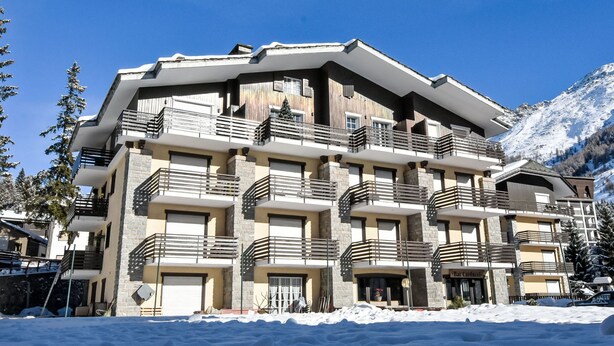 Un hotel de varios pisos con balcones, una pista de esquí al fondo y un paisaje nevado.
