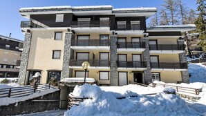 Un hotel de varios pisos con balcones, fachada de piedra y suelo cubierto de nieve.