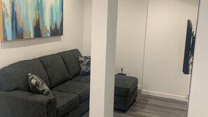 A modern living room with a grey sofa, a small ottoman, and a painting on the wall. - Friendly extended stay and comfort (Winnipeg)