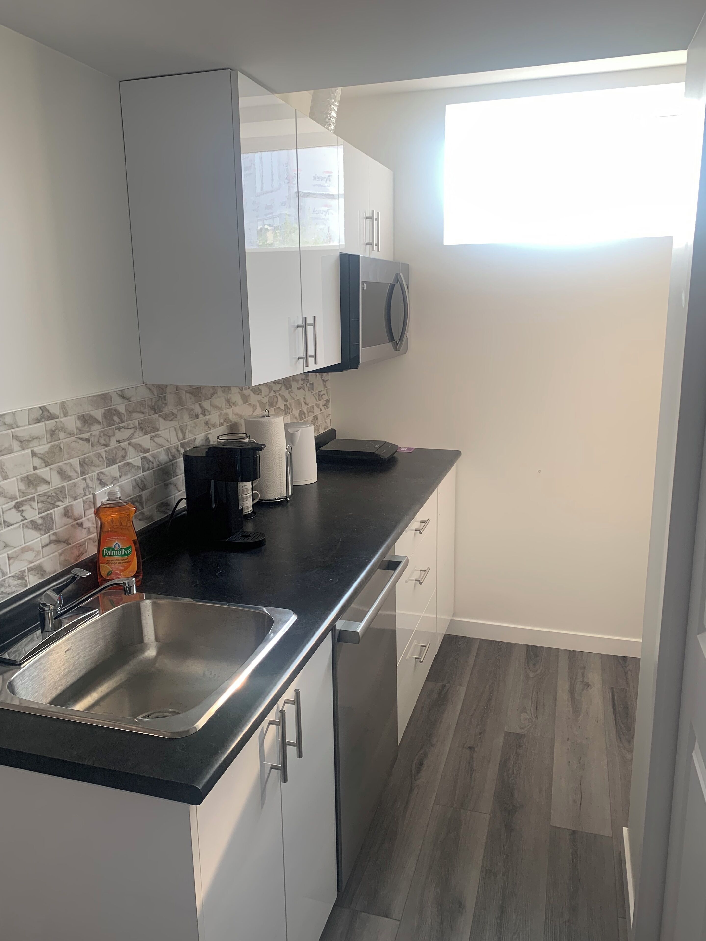 A modern kitchen with a stainless steel sink, white cabinets, a black countertop, and a window providing natural light.