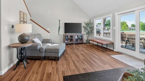 Una sala de estar moderna con un sofá modular, un televisor de pantalla plana, piso de madera y un ventanal con vistas.