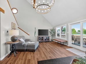 Una sala de estar moderna con un sofá modular, un televisor de pantalla plana, piso de madera y un ventanal con vistas.