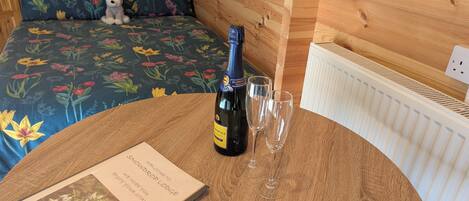 Un lit avec une literie à motifs floraux, une bouteille de champagne, deux verres et un mot de bienvenue posé sur une table en bois.