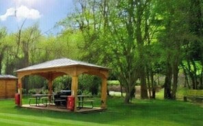 A gazebo with a grill, picnic tables, and a grassy area.