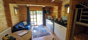Interior de cabana com sala de estar, cozinha compacta e um cão.