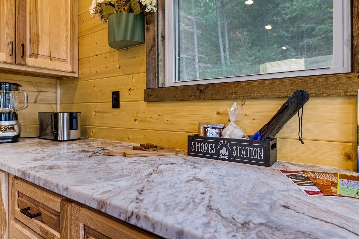 A kitchen with wooden cabinets, a marble countertop, a coffee maker, a kettle, and a sign that reads "S'mores Station".