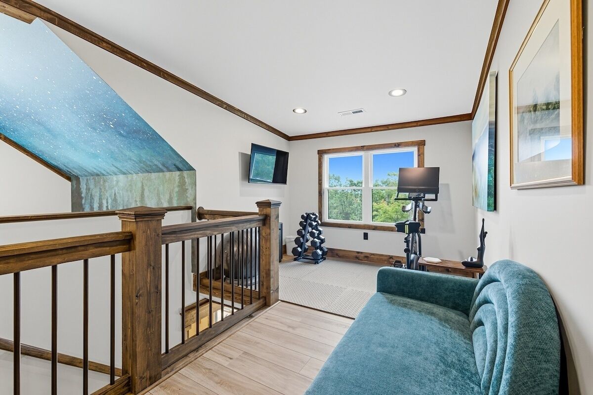 Una habitación amplia con una escalera de madera, un ventanal con vistas, un sofá azul y un techo con un diseño único.